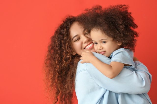 Little African-American girl with her mother on color background